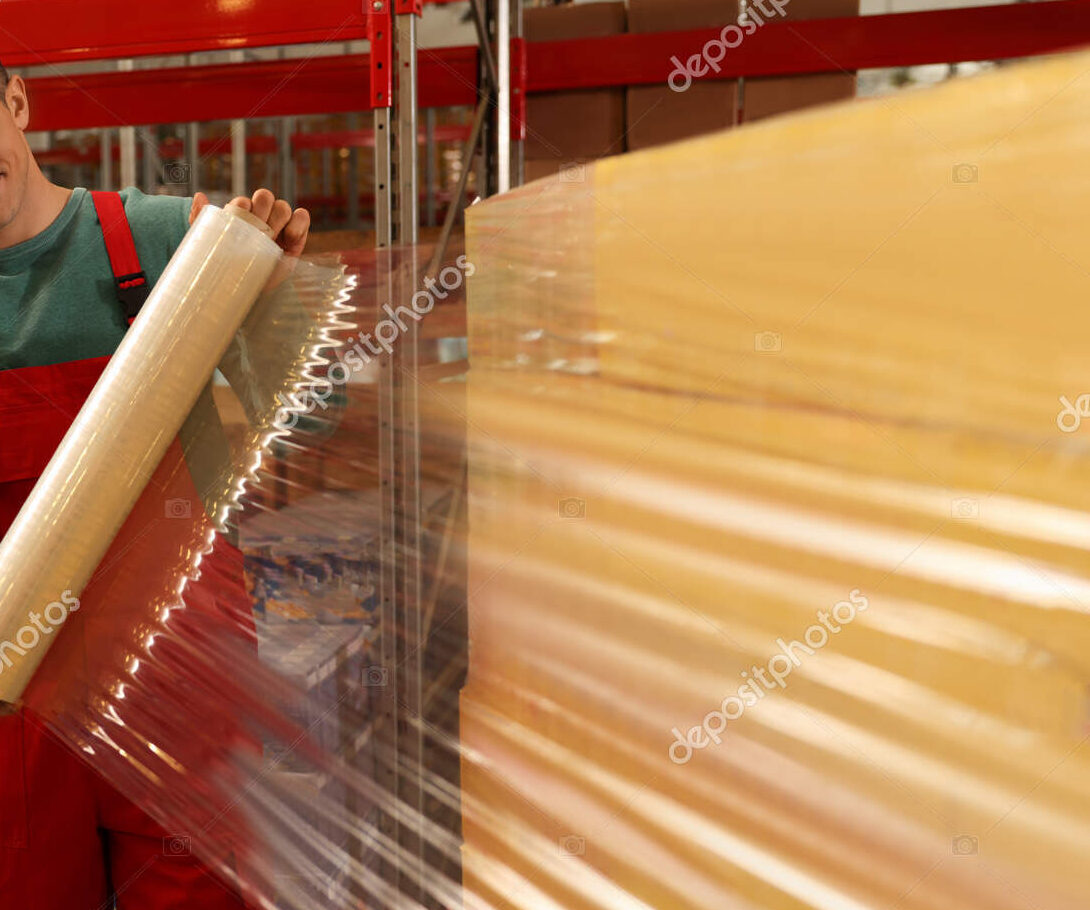 Worker wrapping boxes in stretch film at warehouse